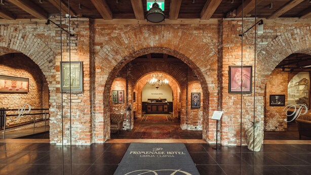 A hotel lobby with a brick archway, a chandelier, and a reception desk.