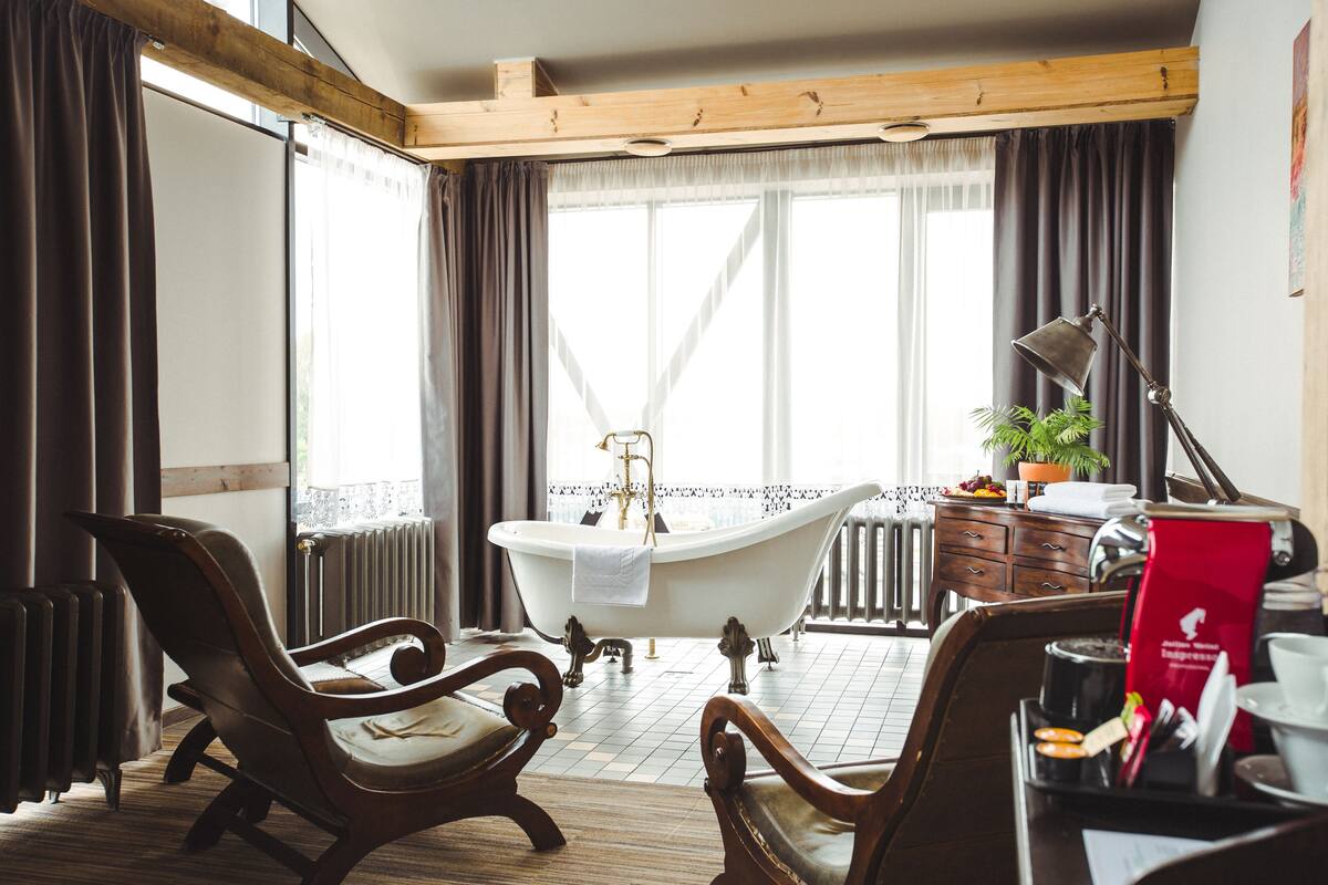 A room with a bathtub, wooden furniture, a radiator, and a window with curtains.