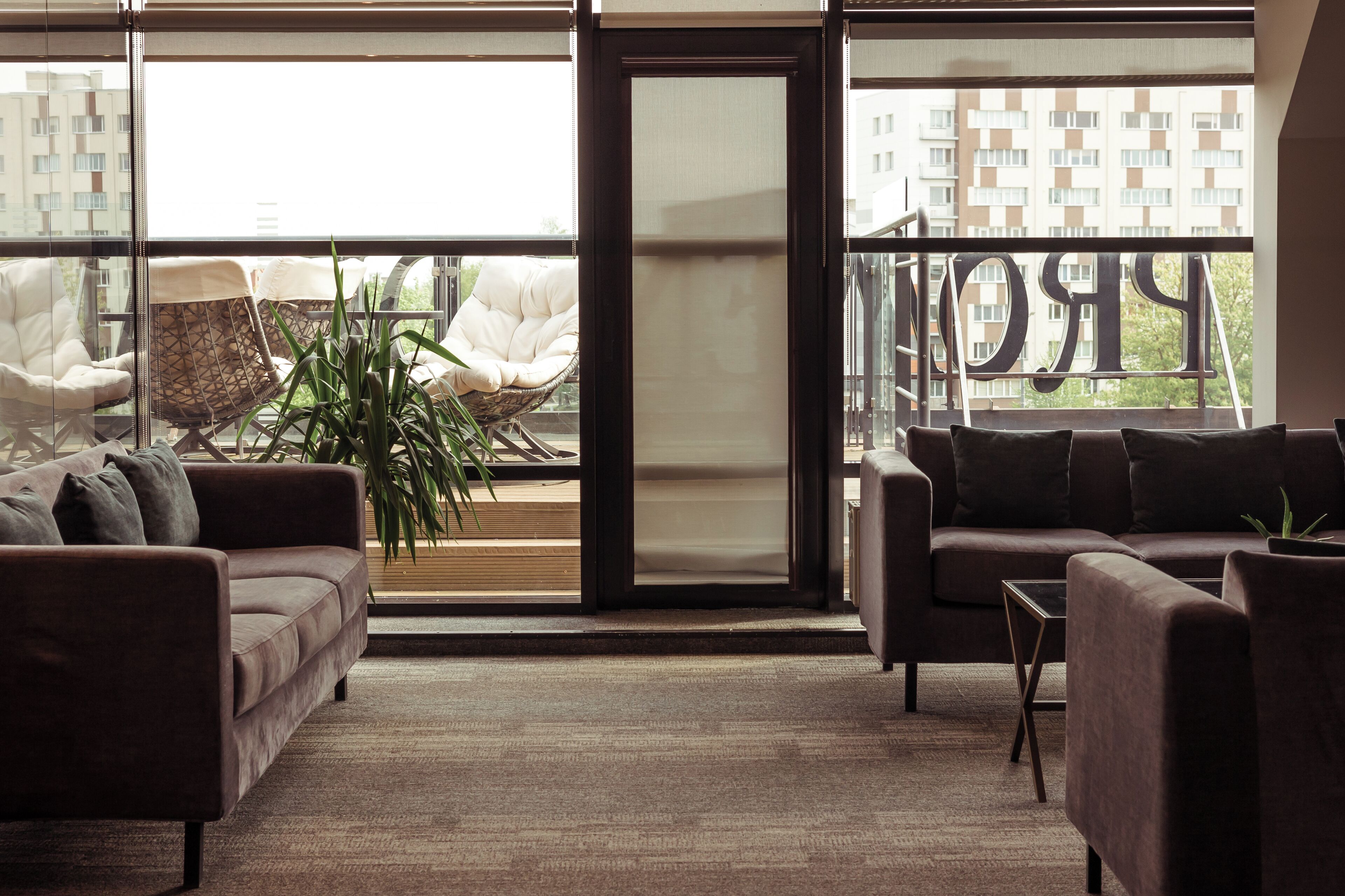 A modern living room with a sofa, armchairs, and a coffee table. Large windows offer a view of a cityscape.
