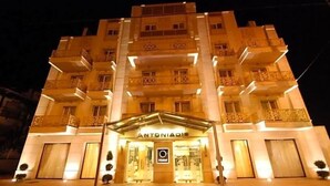 Un hotel a più piani con un ingresso centrale, balconi su ogni piano e una facciata ben illuminata.