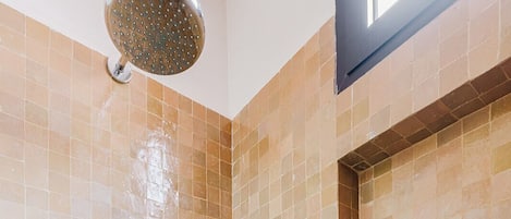 A shower with a handheld showerhead, a wall-mounted faucet, and two bottles of shampoo and conditioner on a shelf.