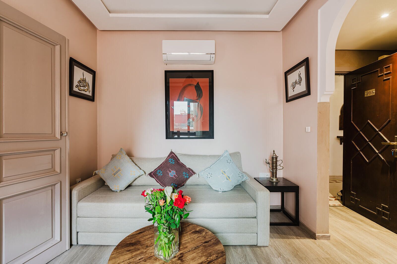 A living room with a sofa, a coffee table with flowers, a framed picture, and a door with a number.