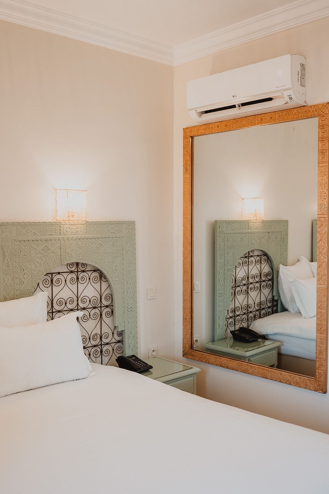 Habitación de hotel con cama, mesita de noche, teléfono y un espejo grande con marco decorativo.