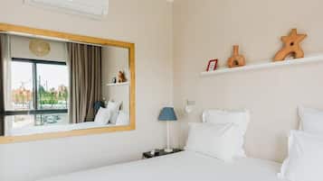 A hotel room with a large bed, a bedside table with a lamp, a mirror, and a shelf with decorative items.