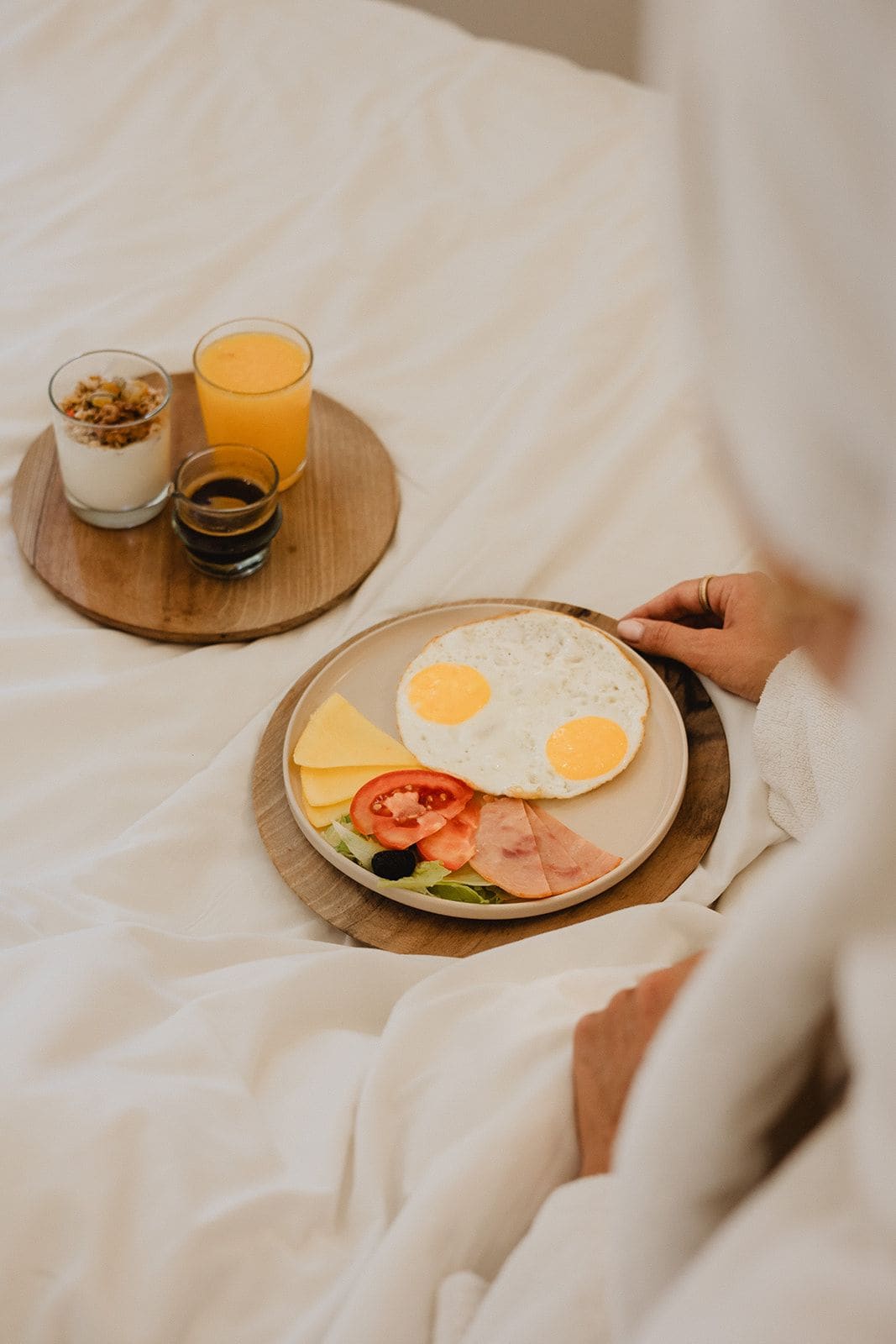 A breakfast tray with eggs, cheese, ham, tomatoes, and a glass of orange juice on a bed.