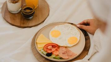 A breakfast tray with eggs, cheese, ham, tomatoes, and a glass of orange juice on a bed.