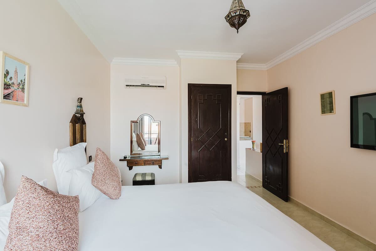 Una habitación de hotel con una cama, un tocador, un espejo, una puerta y un televisor.