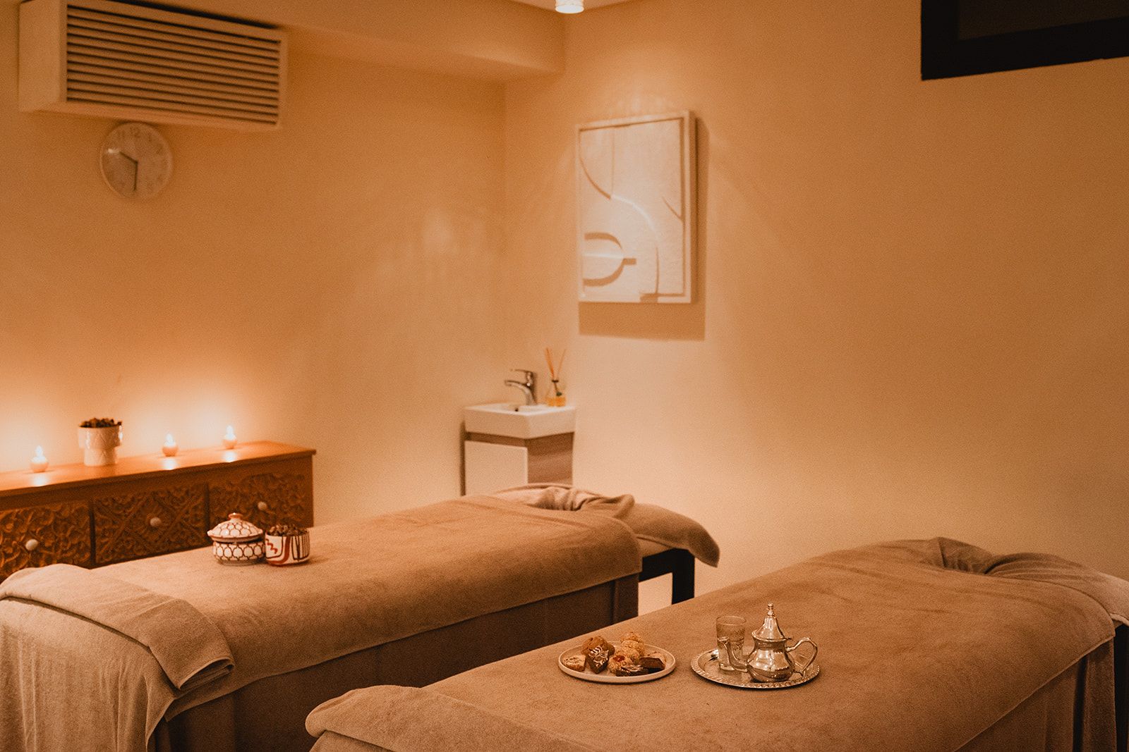 A spa room with two treatment tables, a sink, and a decorative wall piece.