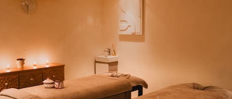 A spa room with two treatment tables, a sink, and a decorative wall piece.