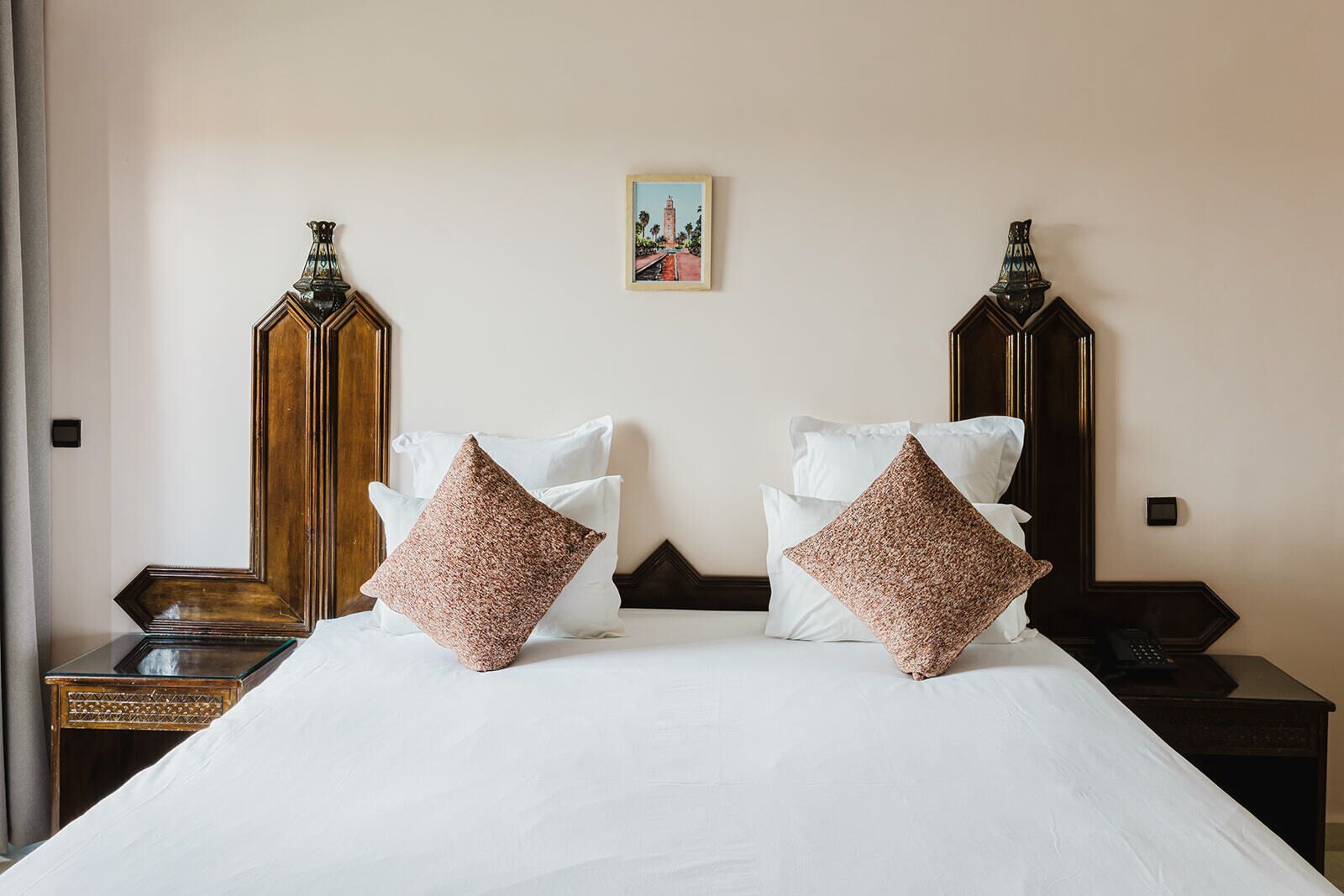 Una habitación de hotel con una cama grande, dos mesitas de noche, un cuadro en la pared y un armario de madera.