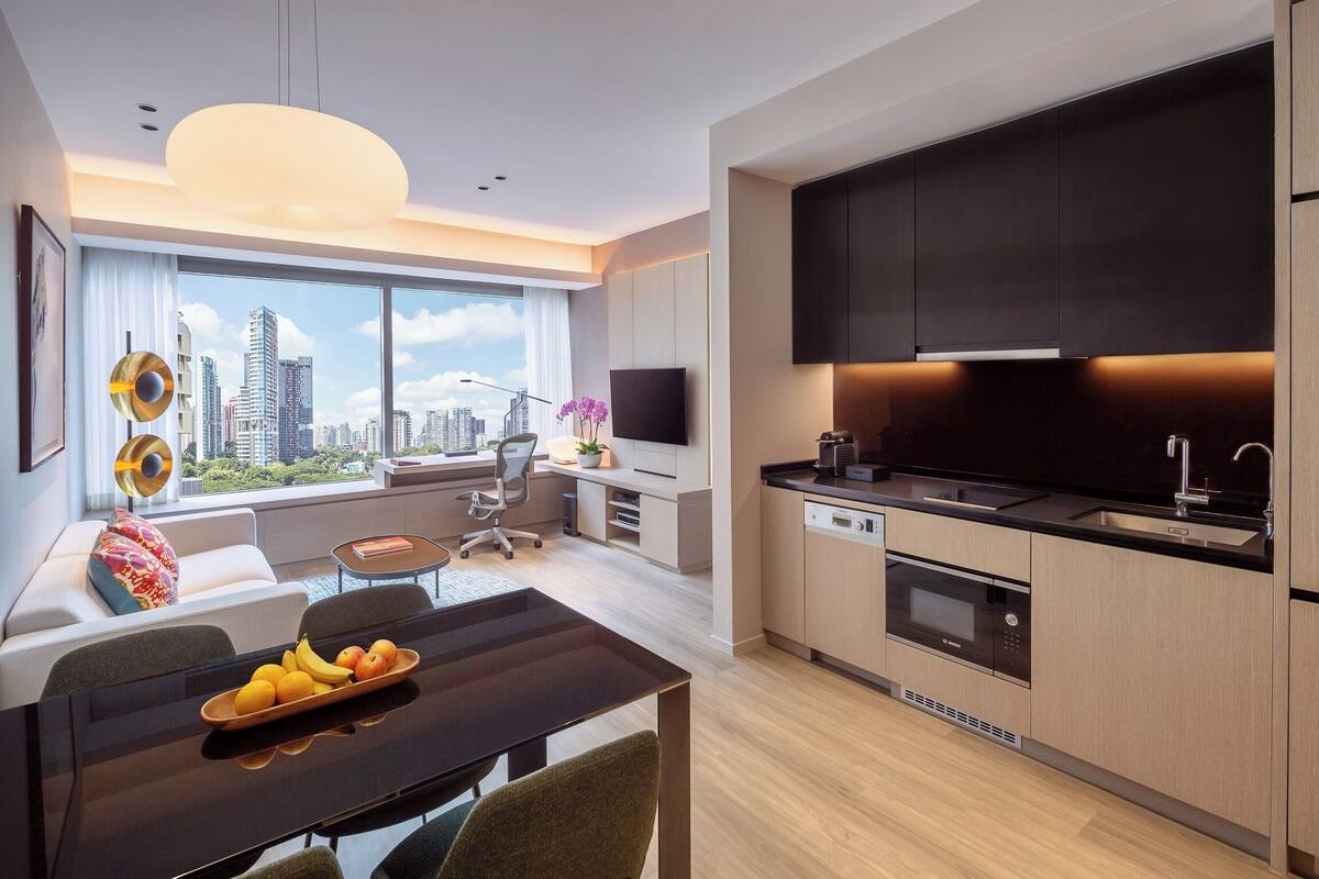 A modern apartment with a dining area, kitchen, and a large window offering a city view.