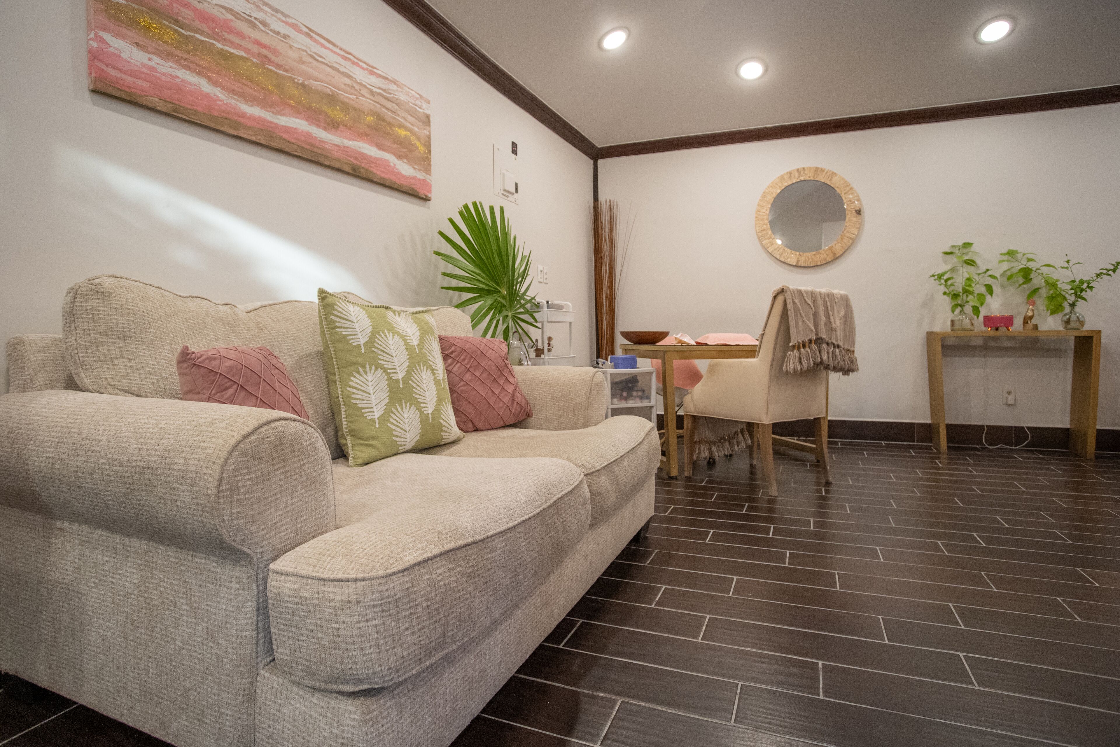 Una sala de estar con un sofá color beige, una mesa de centro, un espejo redondo y una planta en maceta.