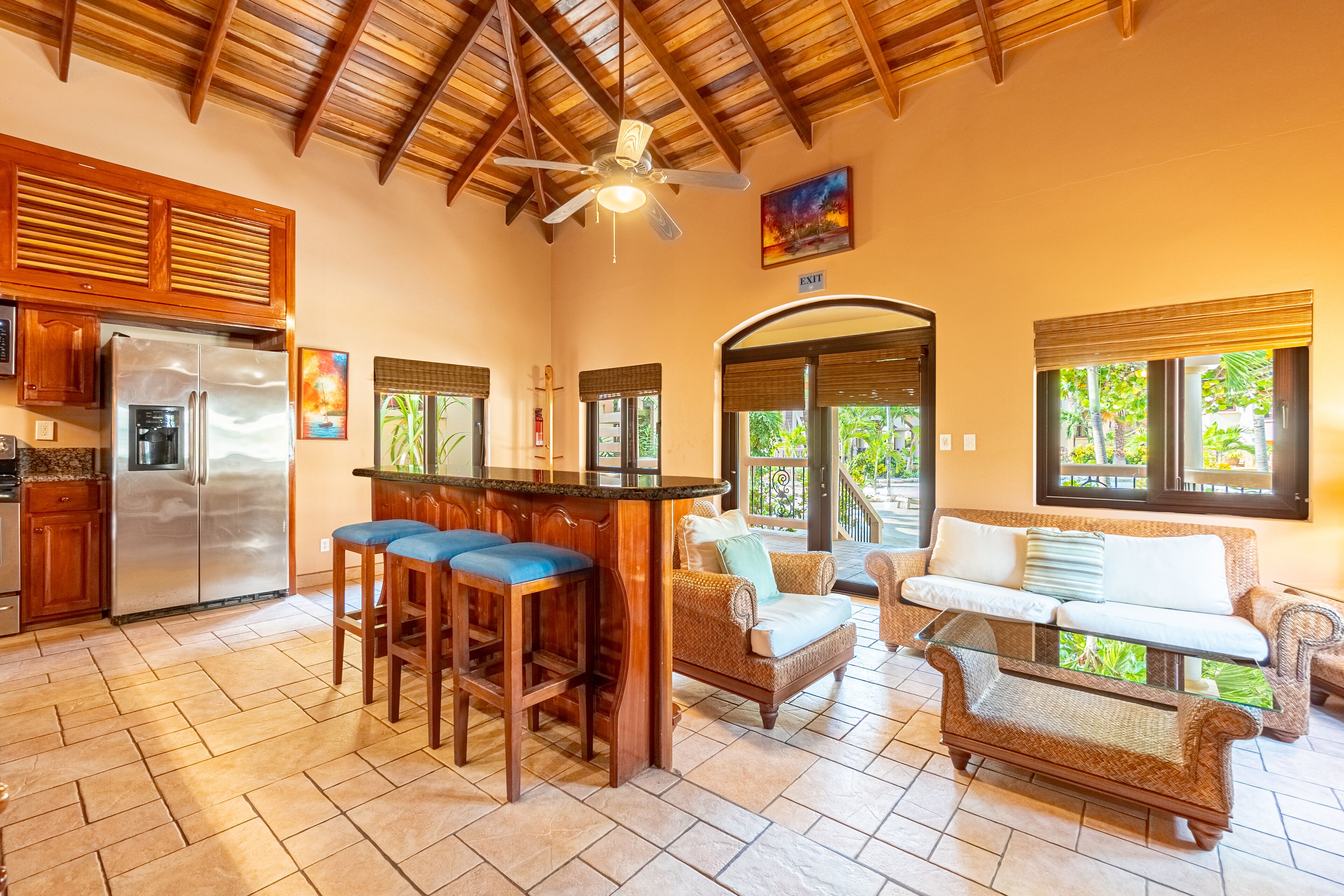 A kitchen with a central island, bar stools, and a refrigerator. There is a seating area with a sofa and chairs.