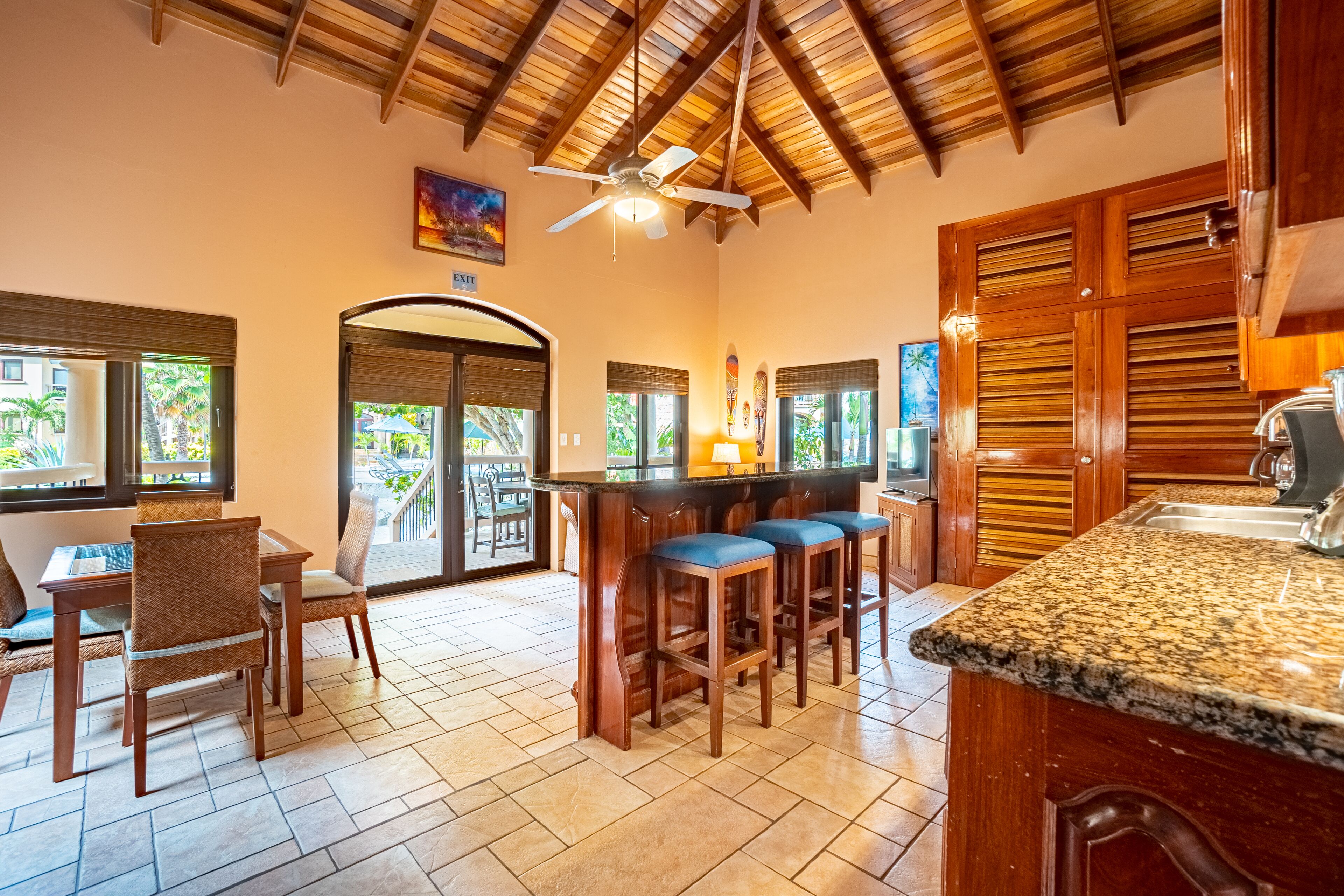 A spacious kitchen with a bar area, wooden ceiling, and large windows.