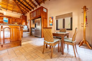 A kitchen with wooden cabinets, a refrigerator, a dining table with chairs, and a window with a view.