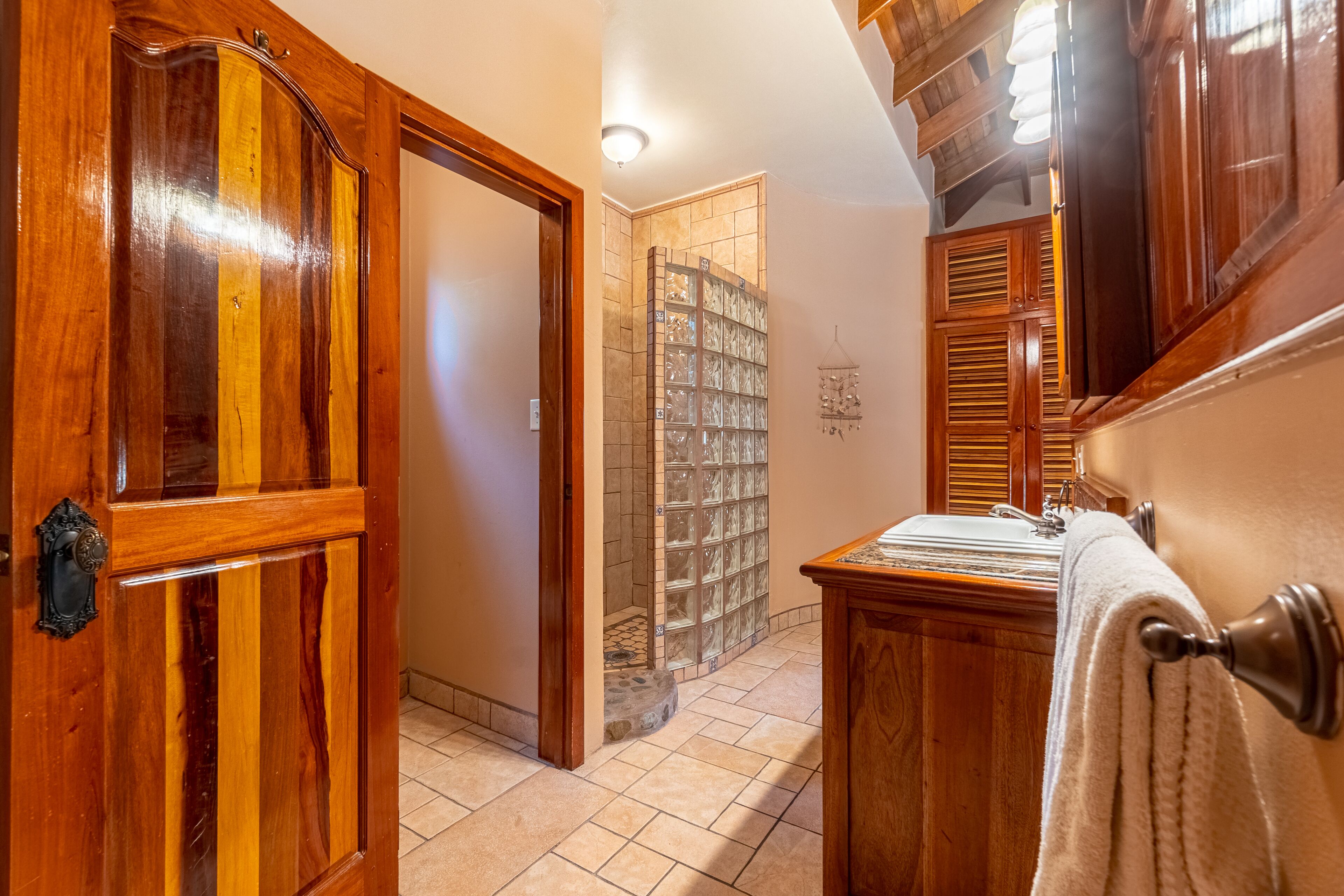 A wooden hallway with a door, a tiled floor, and a stone wall with a glass door.