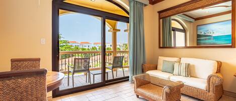 A spacious balcony with a view of a coastal area, furnished with wicker furniture and a glass table.