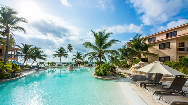 Une piscine d’un complexe hôtelier, avec une eau cristalline, entourée de palmiers et de chaises longues.