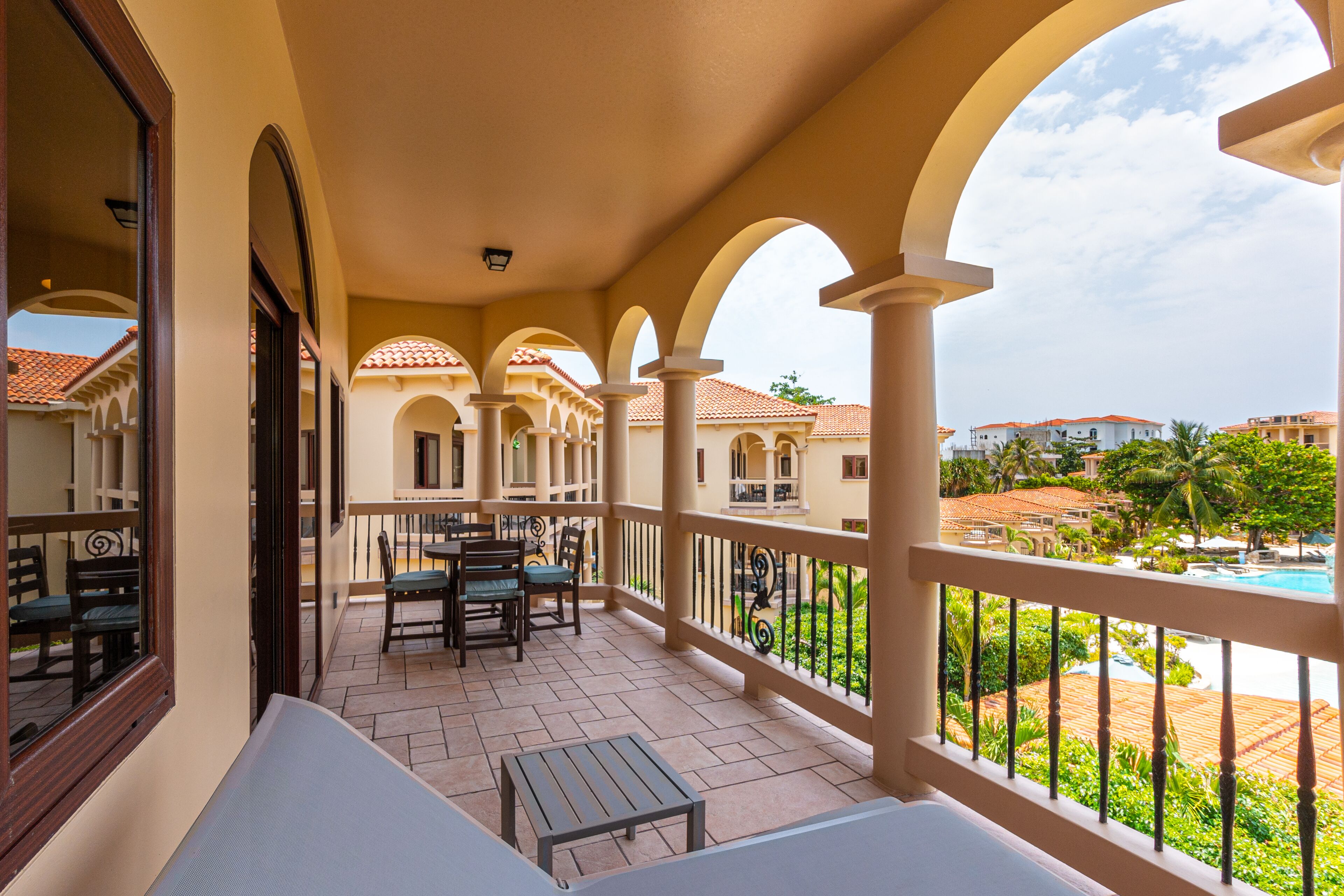 A balcony with a table and chairs, a pool view, and a building with arches.