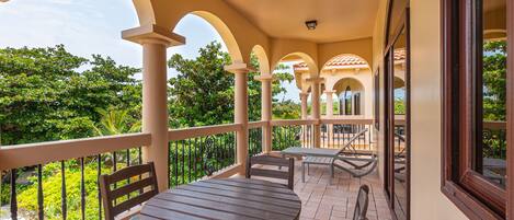 A covered outdoor patio with a round table and chairs, surrounded by arches and a railing.