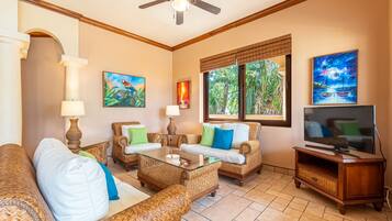 A living room with wicker furniture, a glass coffee table, a TV, and artwork on the walls.