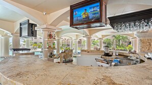 Un espace bar doté d’un écran de télévision, de plans de comptoir en marbre et d’une piscine en arrière-plan.