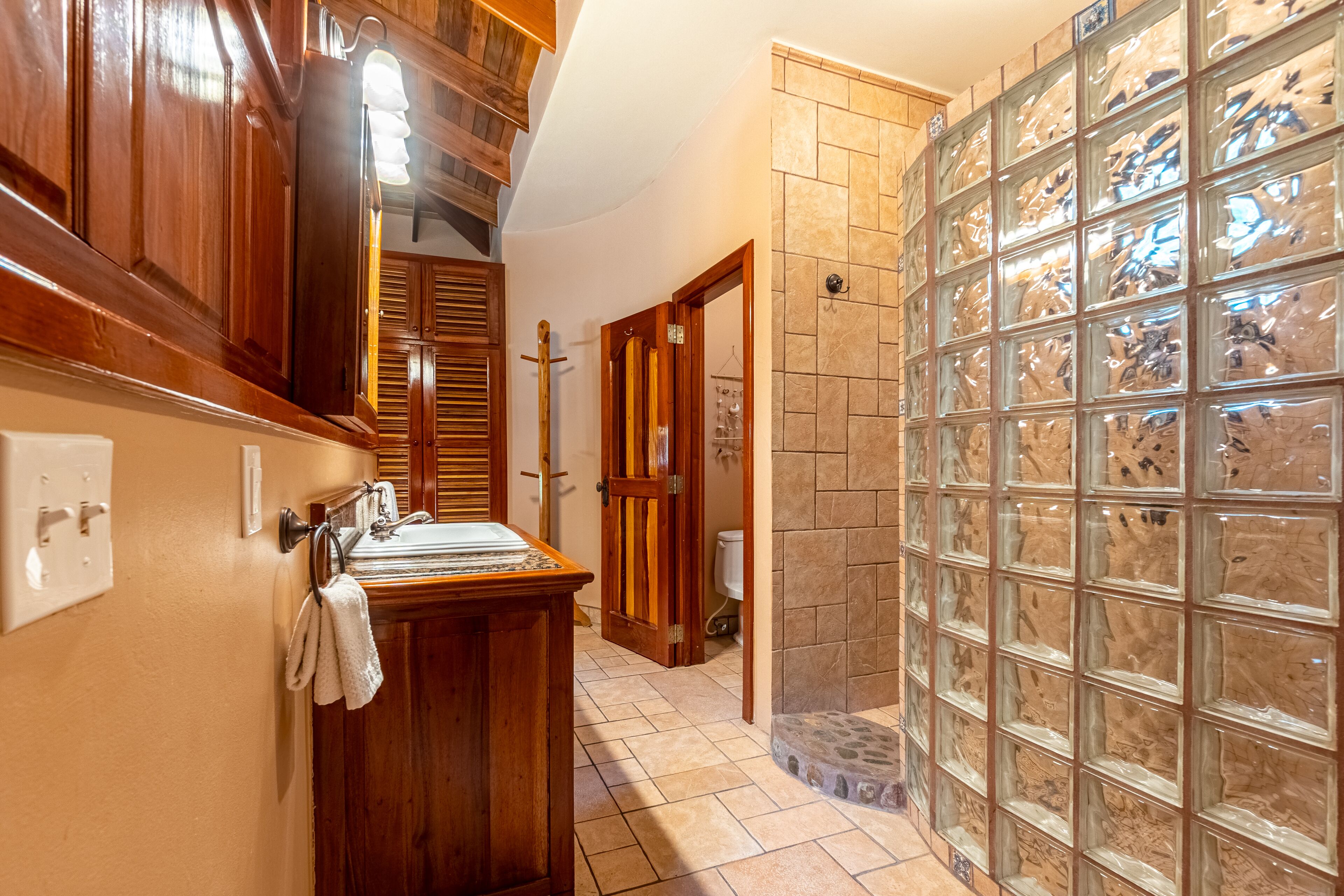 A bathroom with wooden cabinets, a glass shower enclosure, and a tiled floor.