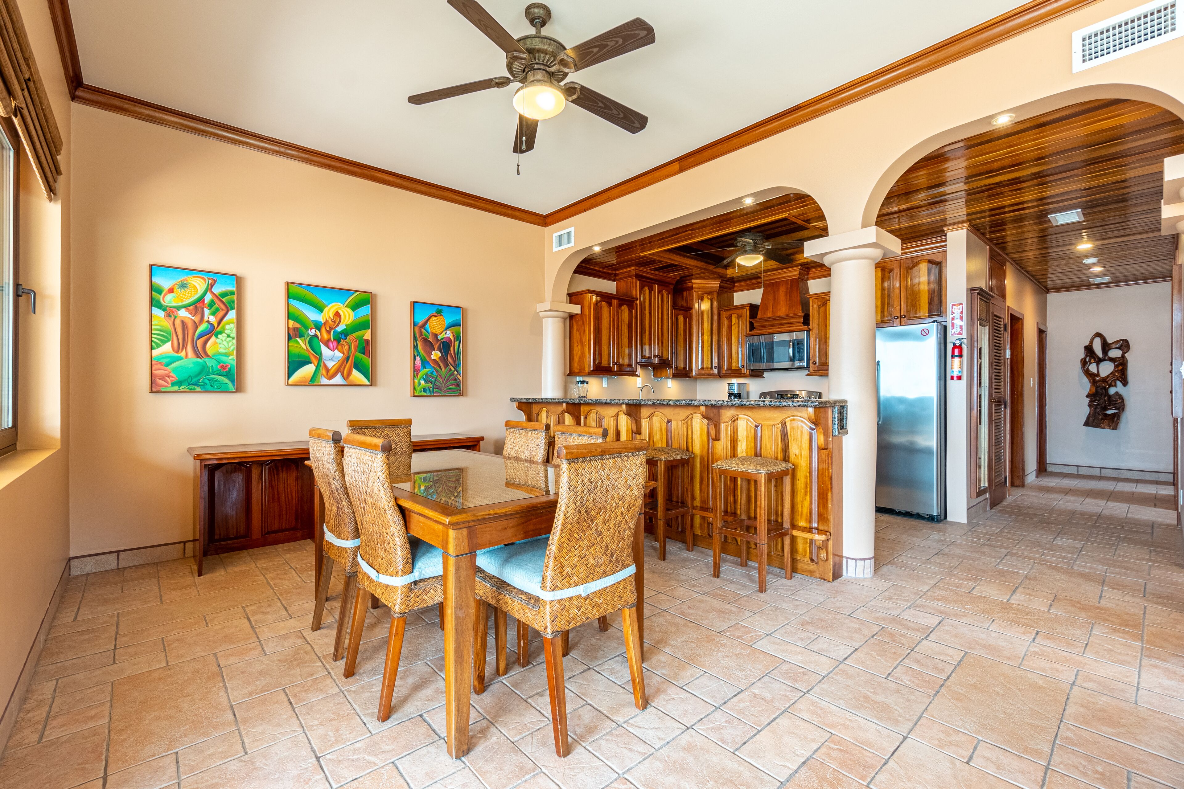 A spacious kitchen with wooden cabinets, a central island, and a dining area with wicker chairs.