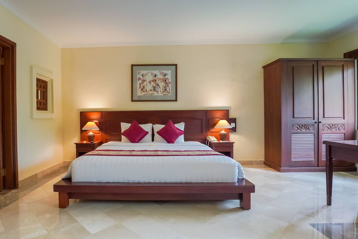 Ein Hotelzimmer mit einem großen Bett, zwei Nachttischlampen, einem Holzkopfstück, einem gerahmten Bild über dem Bett und einem Kleiderschrank mit Spiegel.