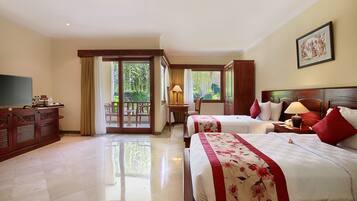 A hotel room with two beds, a TV, a desk, and a balcony with a view of greenery.