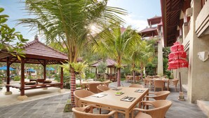 An outdoor patio area with wicker furniture, stone flooring, and a mix of palm trees and traditional architecture. - The Grand Bali Nusa Dua (Nusa Dua)