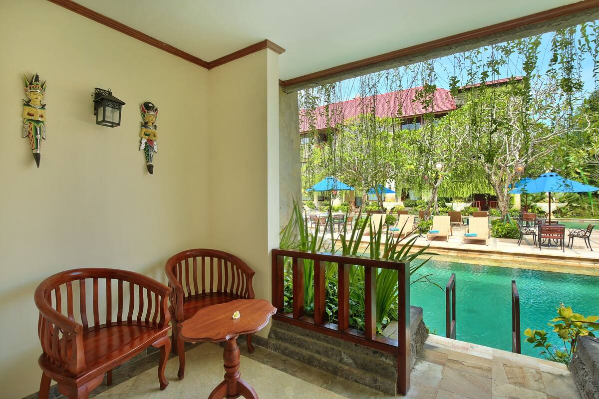Ein Balkon mit Holzkubeln und Tisch, mit Blick auf einen Swimmingpool und eine Sitzgelegenheit im Freien mit Sonnenschirmen.
