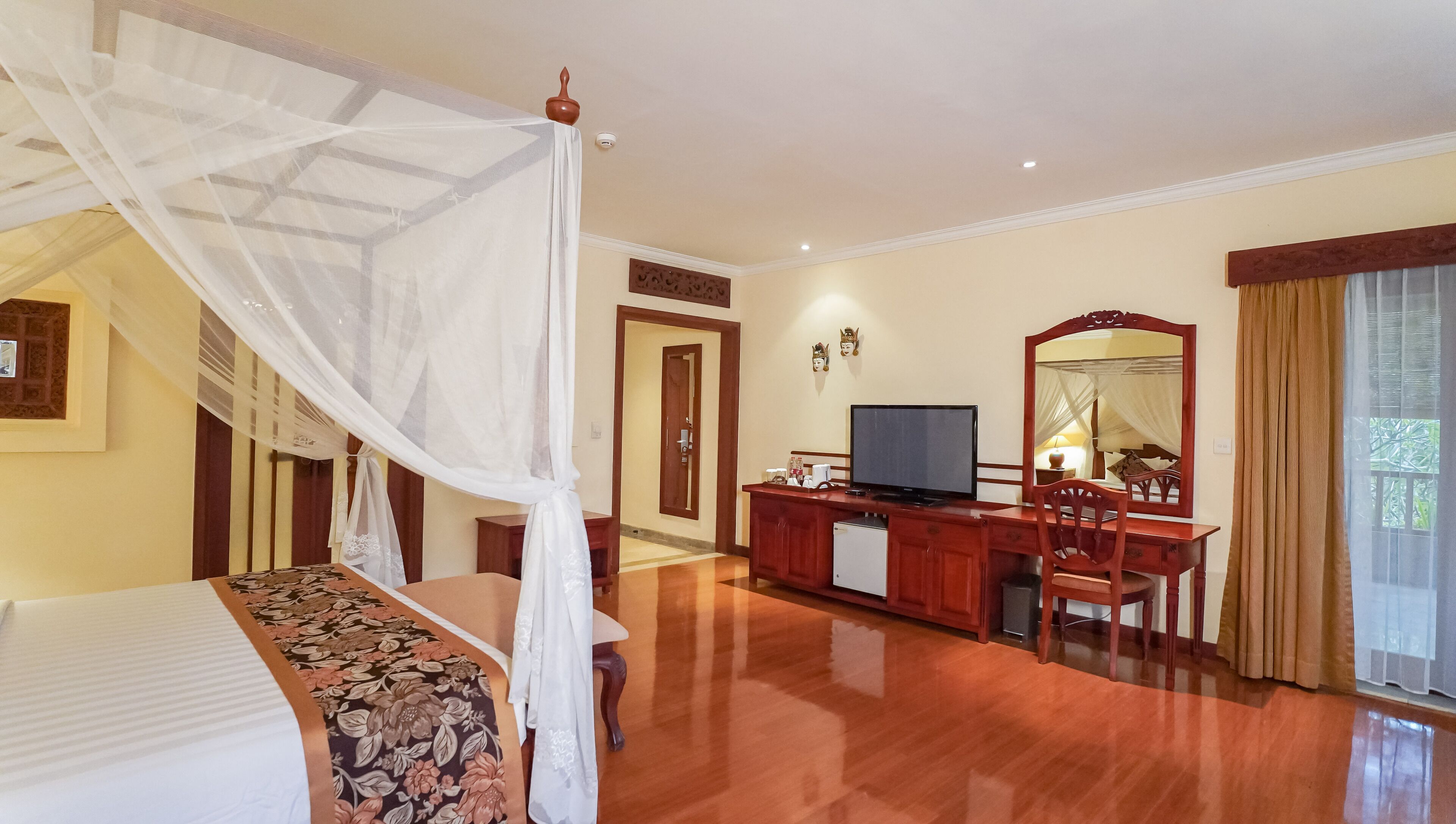 A hotel room with a bed, a desk with a television, a mirror, and a window with curtains.