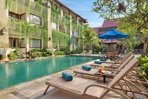 A poolside area with lounge chairs, a pool, and a building with balconies covered in greenery. - The Grand Bali Nusa Dua (Nusa Dua)