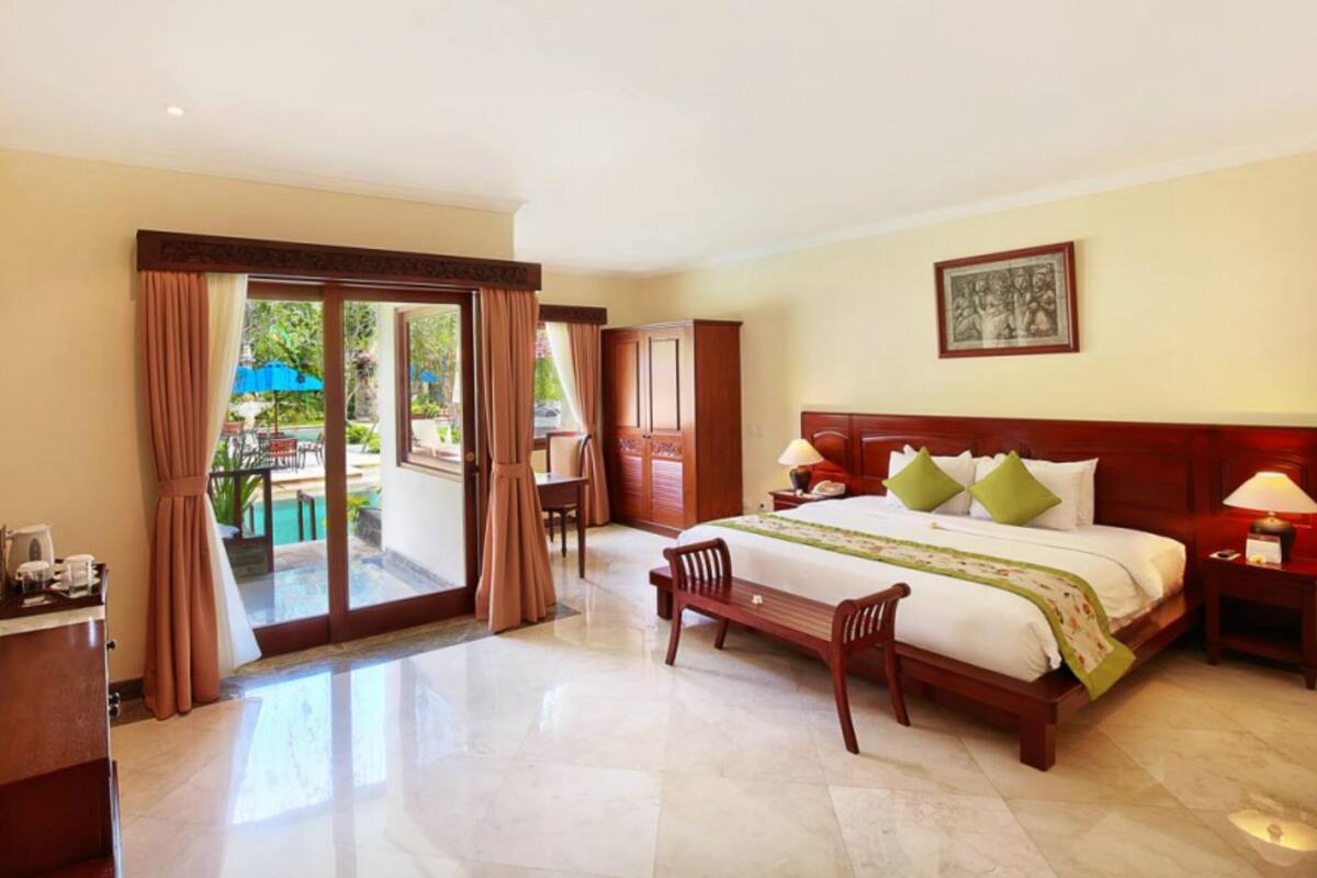 A hotel room with a bed, a desk, a chair, a TV, and a view of the outside.