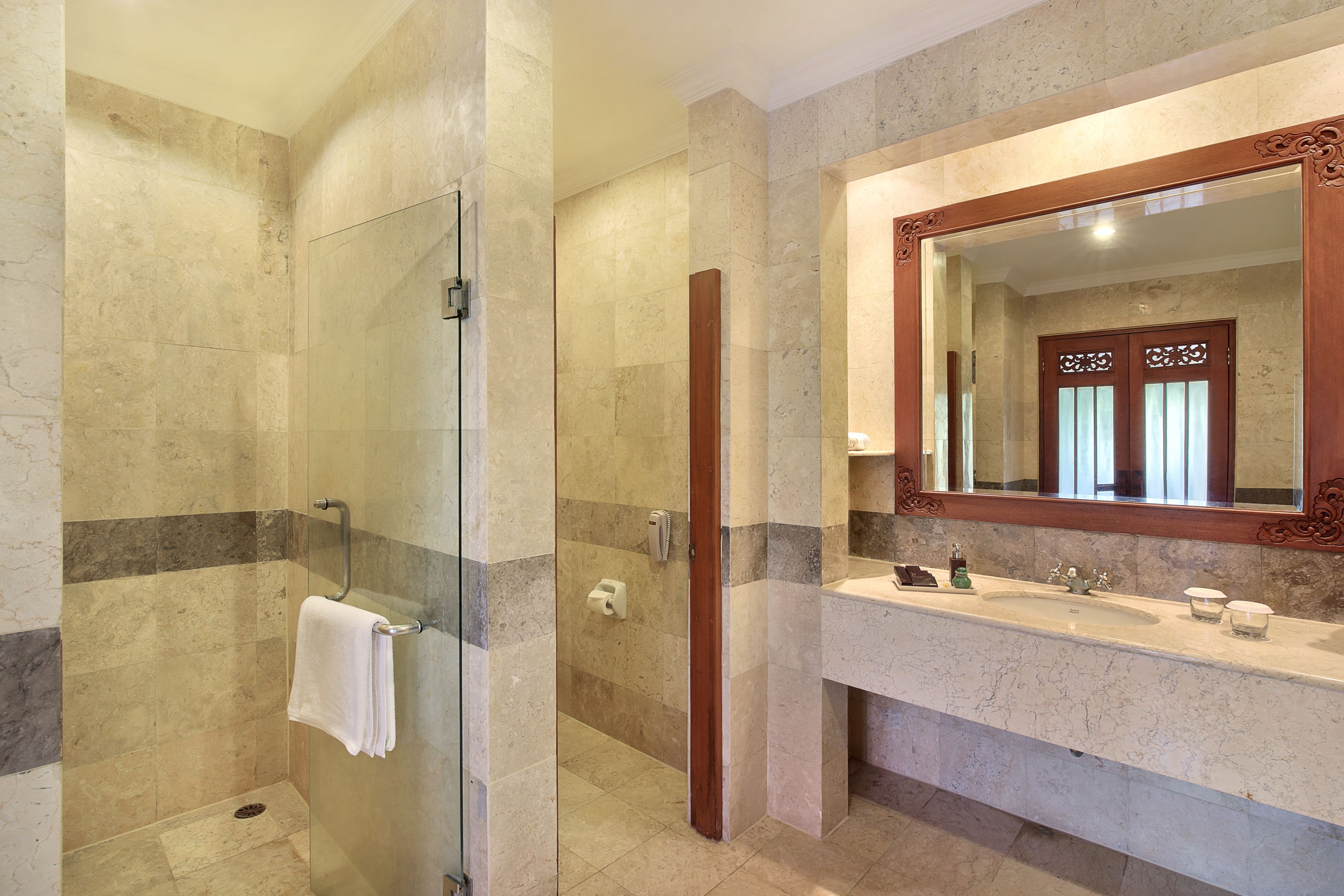 A modern bathroom with a glass-enclosed shower, a marble-tiled wall, and a large mirror above a sink.