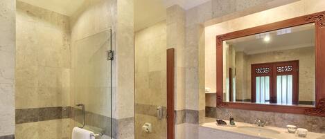 A modern bathroom with a glass-enclosed shower, a marble-tiled wall, and a large mirror above a sink.