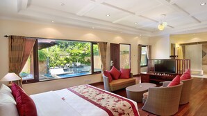 A hotel room with a large bed, a TV, wicker furniture, and a view of greenery outside. - The Grand Bali Nusa Dua (Nusa Dua)