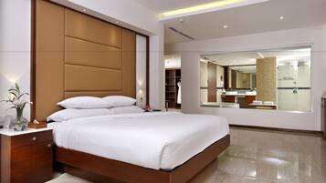 A modern hotel room with a large bed, wooden headboard, bedside tables, a mirror, and a bathroom visible through an open door.