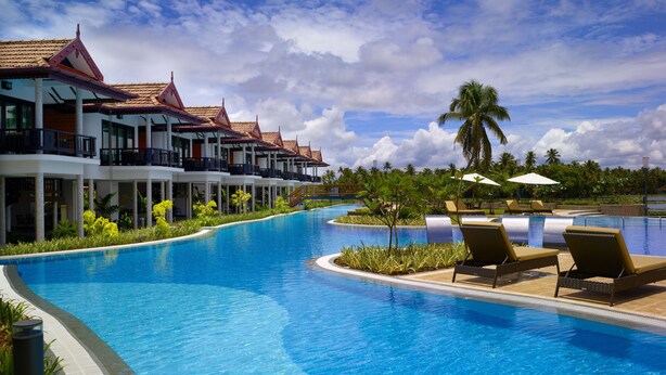 A resort with a large swimming pool, multiple-story buildings with balconies, and palm trees. - Ramada Resort by Wyndham Kochi (Kanayannur)