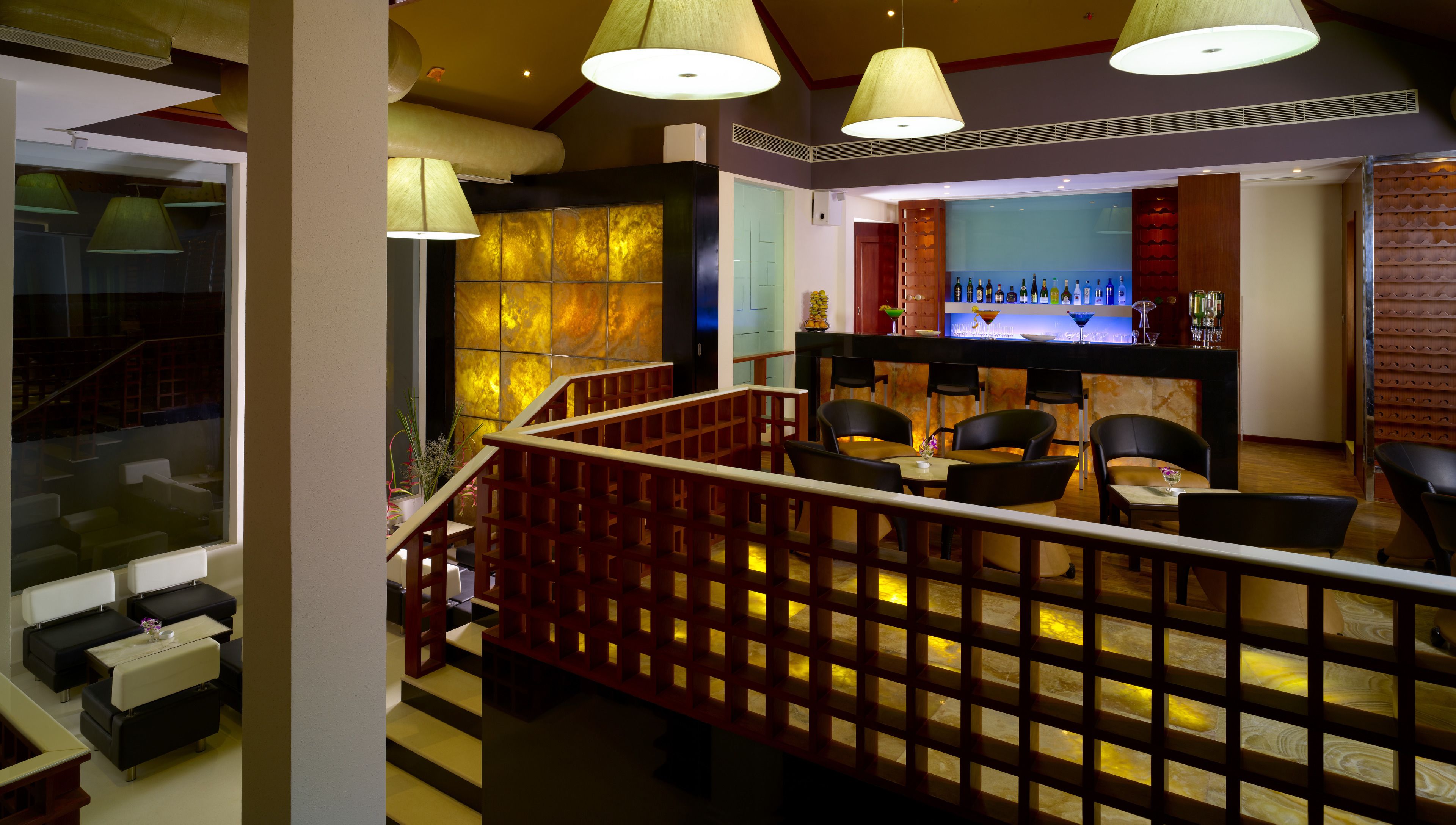 A restaurant with a bar, wooden furniture, and hanging lamps.