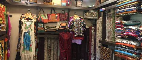 Una boutique con diversos textiles, incluyendo telas estampadas y prendas de vestir exhibidas en estantes y perchas.