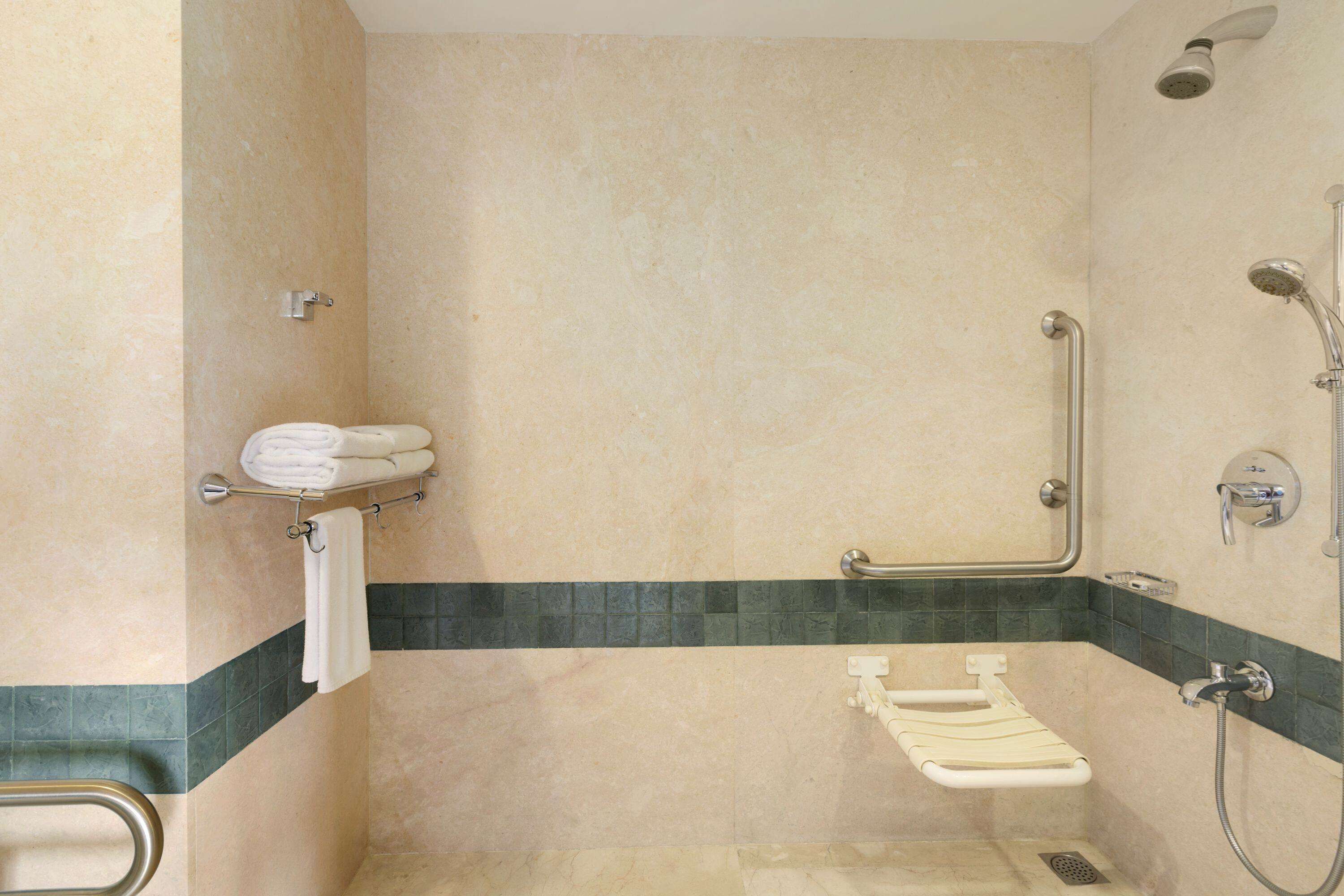 Un bagno con doccia, maniglie di sostegno, porta asciugamani e corrimano.