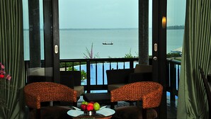 A balcony with two wicker chairs, a small table with fruit, and a view of the sea with a boat. - Ramada Resort by Wyndham Kochi (Kanayannur)