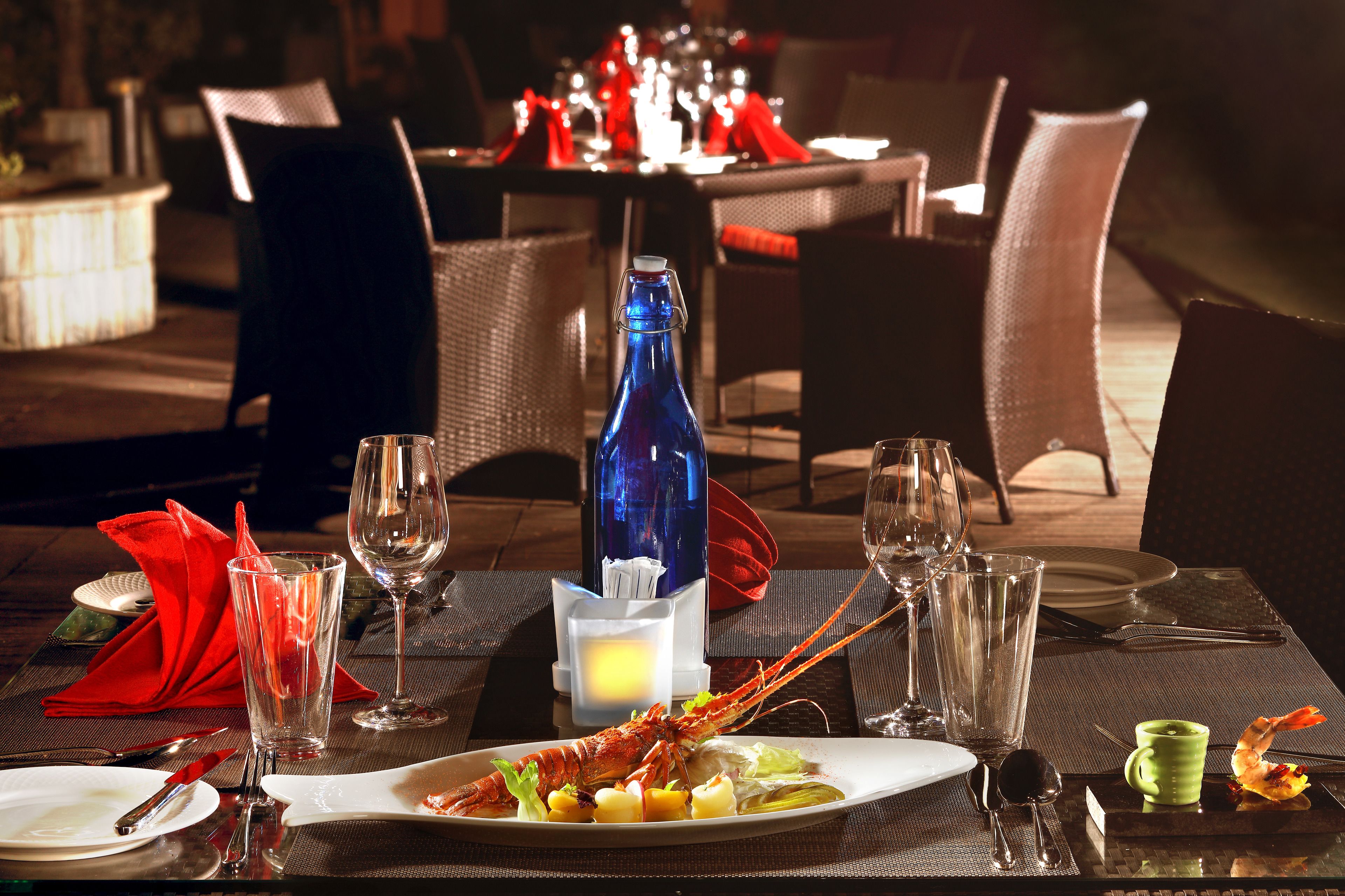 A dining table set with a lobster, wine glasses, and a blue bottle.