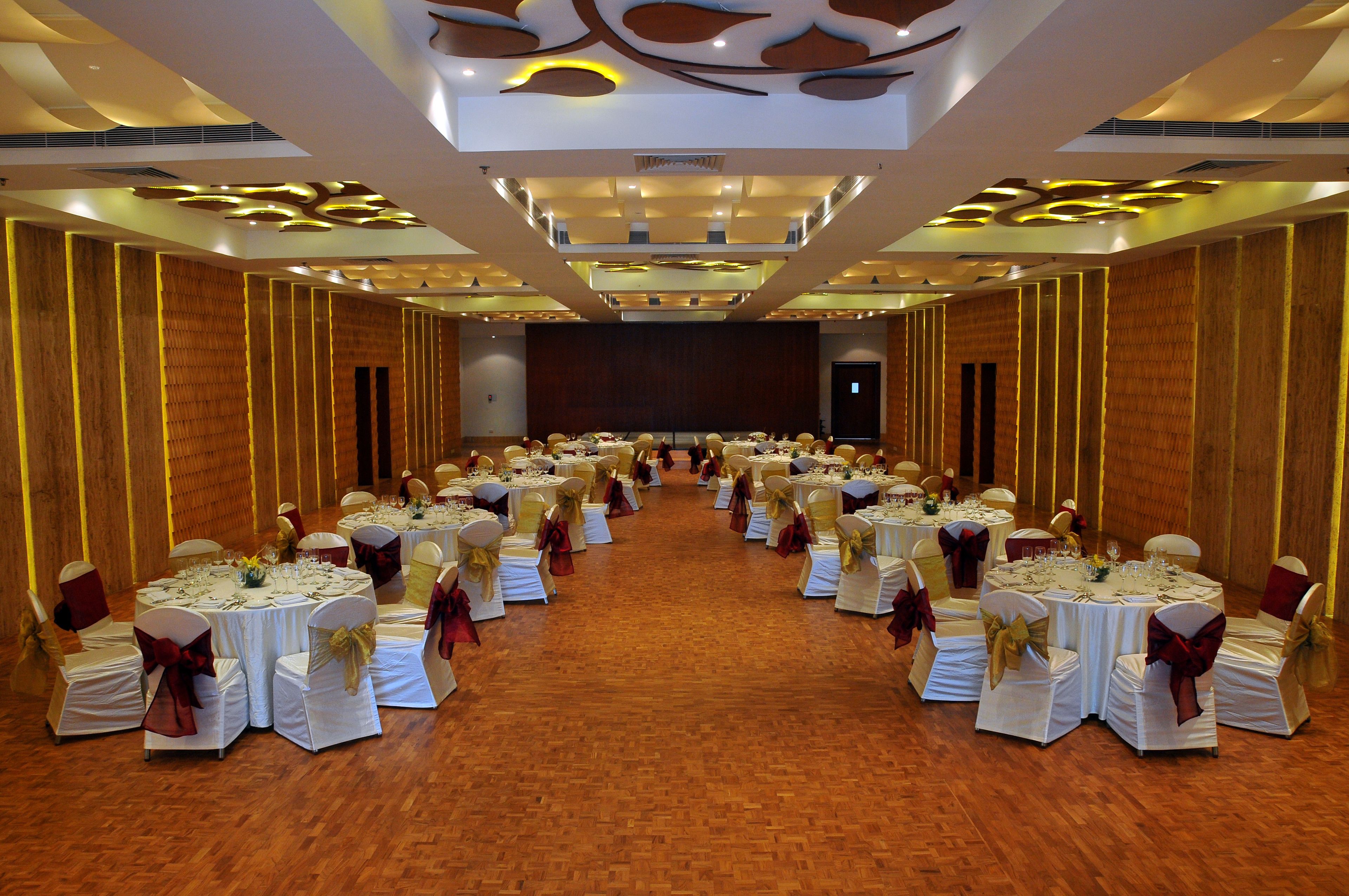 A banquet hall with round tables set for a formal event, featuring white tablecloths and gold sashes.