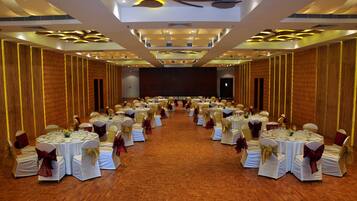 A banquet hall with round tables set for a formal event, featuring white tablecloths and gold sashes.