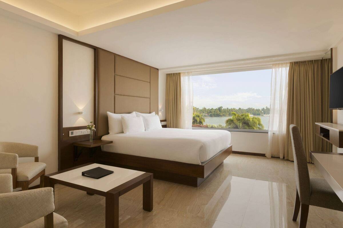 Quarto de hotel com uma cama grande, uma escrivaninha, uma cadeira e vista para um lago.