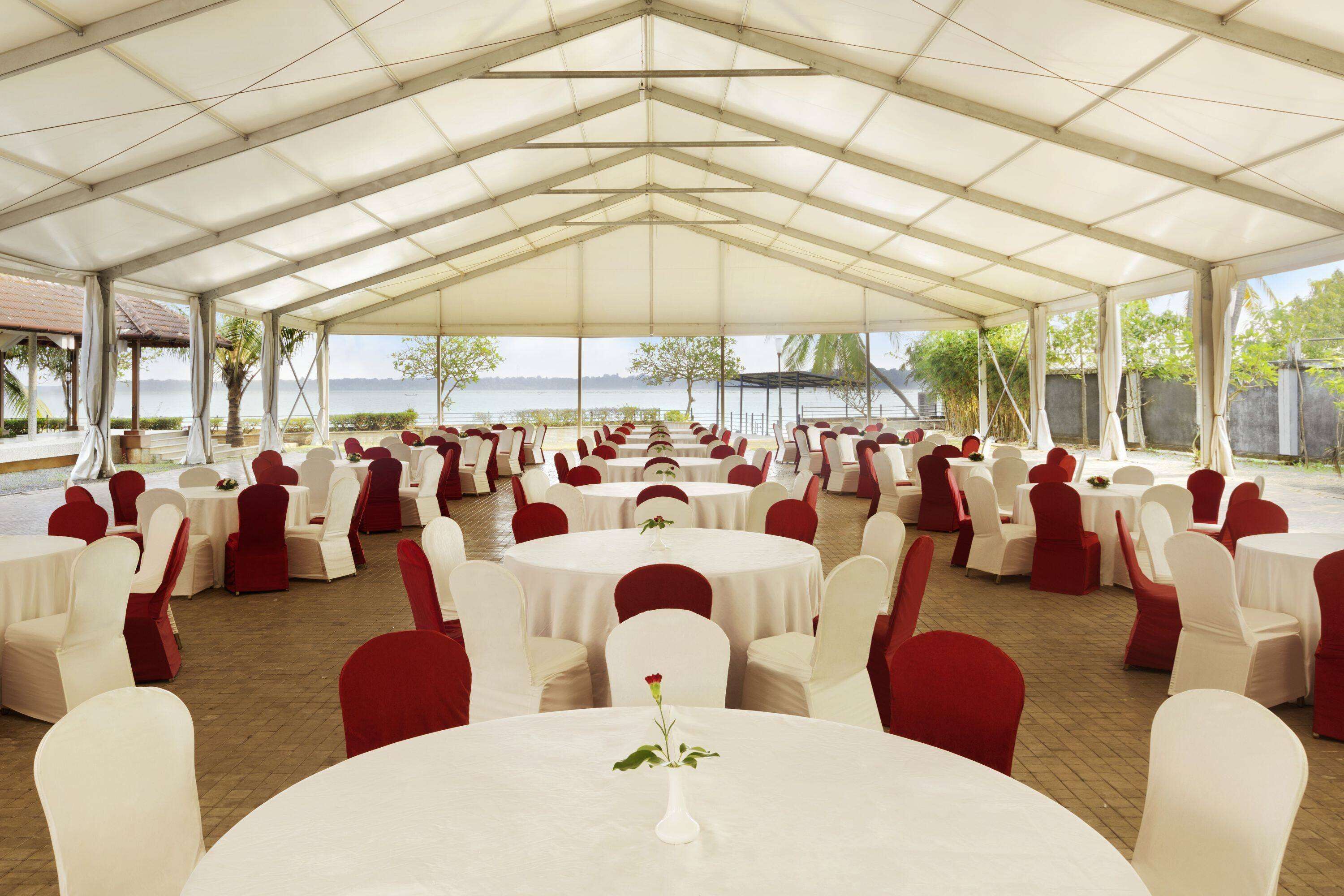 A covered outdoor event space with round tables and chairs, a view of the sea, and a brick floor.