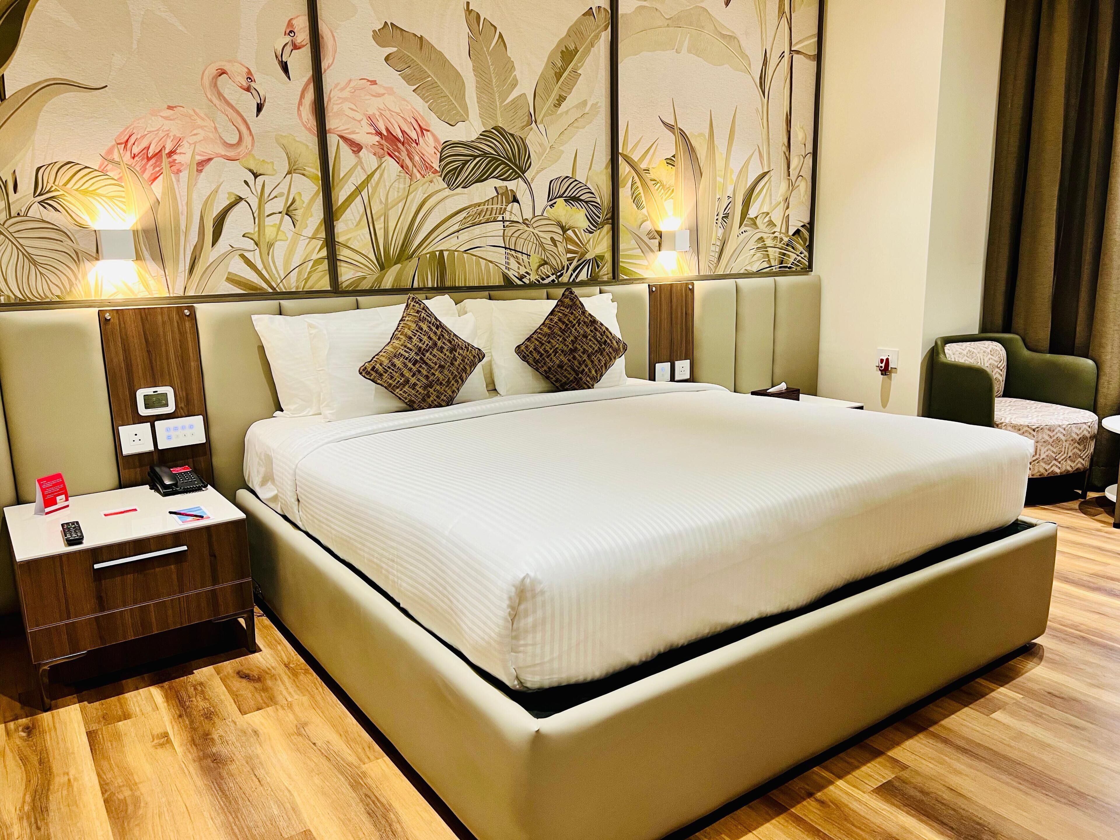 A spacious hotel room with a large bed, a nightstand, a desk, and a chair.